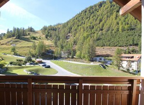 Un balcón con vistas a un paisaje rural, que incluye una carretera, casas y una colina boscosa.