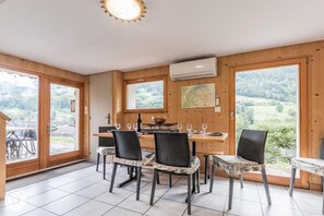 Un comedor con una mesa y sillas de madera, un mapa en la pared y vistas al campo a través de amplios ventanales.