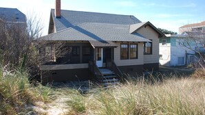 A two-story house with a sloped roof, a front porch, and a chimney. - Rustic Beach Front Apartment - Cozy, Rustic and On the Beach! - 2 BR/1 Bath (Norfolk)