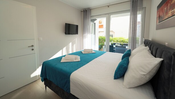 A hotel room with a bed, a TV mounted on the wall, and a sliding glass door leading to an outdoor area. - Apartment near the beach with Patio and Garden (Novalja)