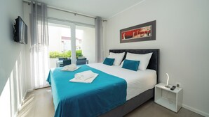 A modern hotel room with a large bed, a flat-screen TV, a bedside table with a lamp, and a view of the outdoors. - Apartment near the beach with Patio and Garden (Novalja)