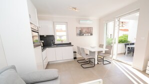 A modern kitchen with white cabinets, a dining area with a table and chairs, and a sliding glass door leading to an outdoor area. - Apartment near the beach with Patio and Garden (Novalja)