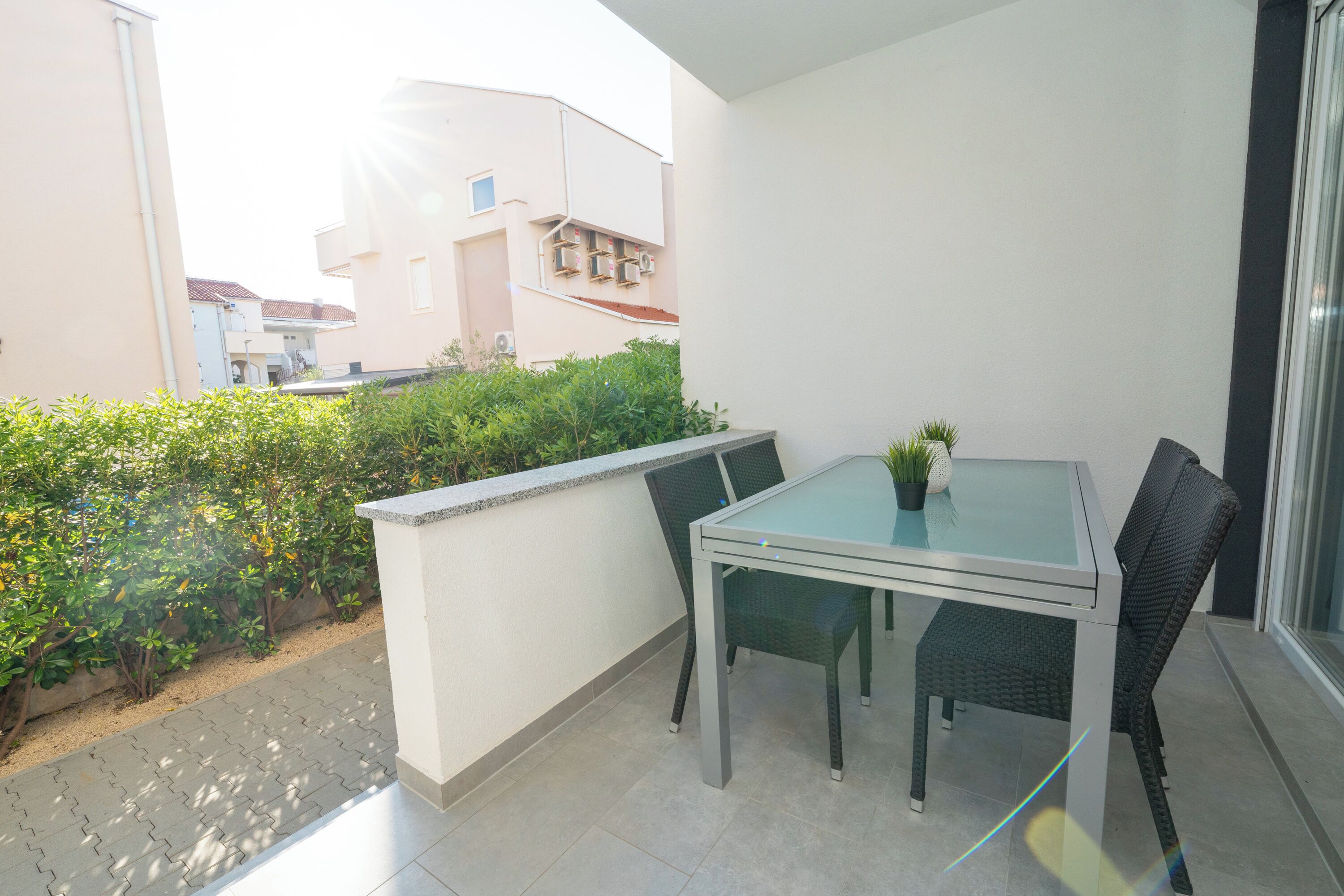 A balcony with a glass table and chairs, a potted plant, and a view of neighboring buildings.