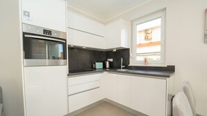A modern kitchen with white cabinets, a built-in oven, a window with a view, and a black countertop. - Apartment near the beach with Patio and Garden (Novalja)