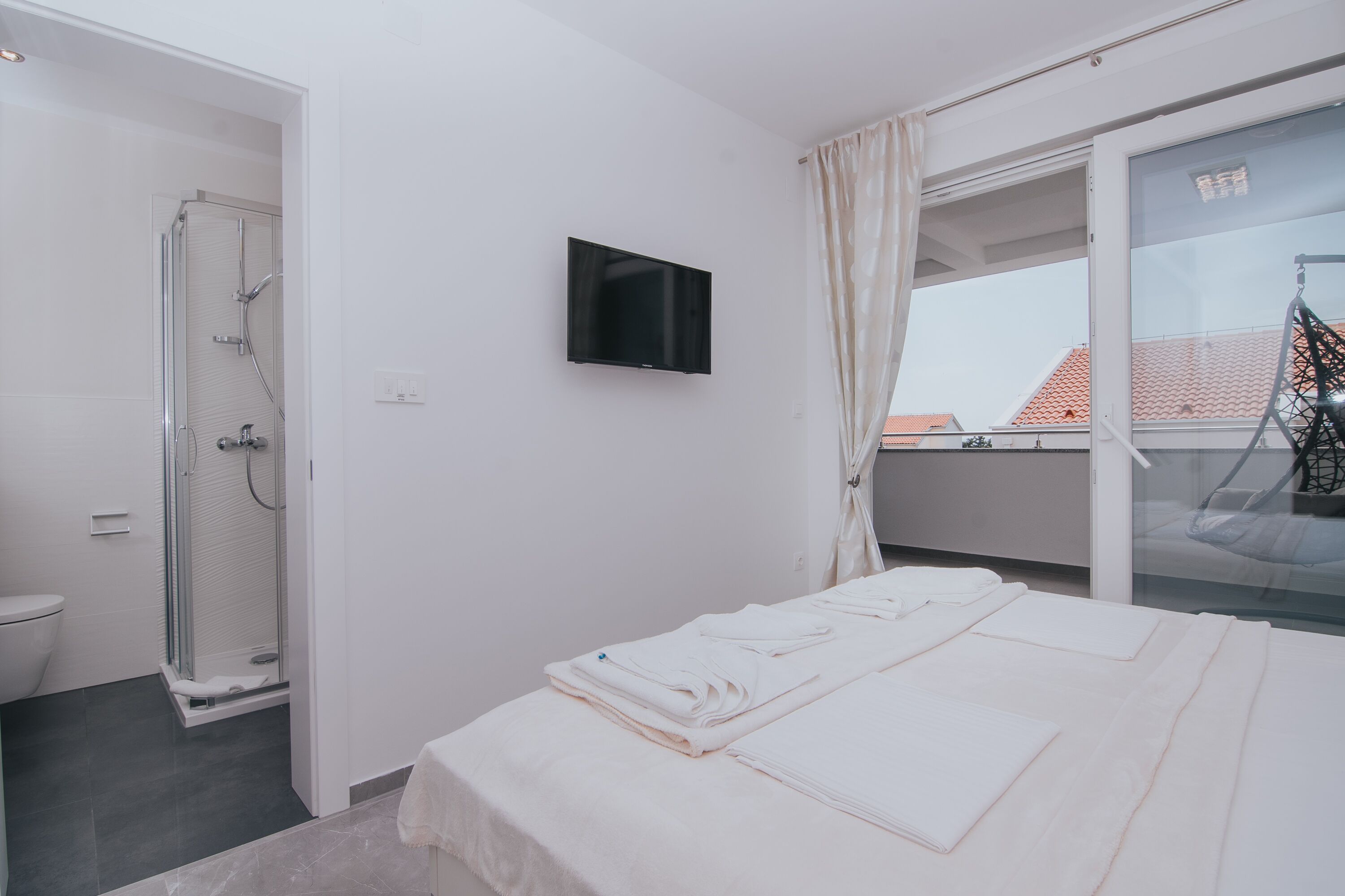 Ein Hotelzimmer mit Bett, Fernseher, Dusche und einem Balkon mit Blick auf Gebäude.