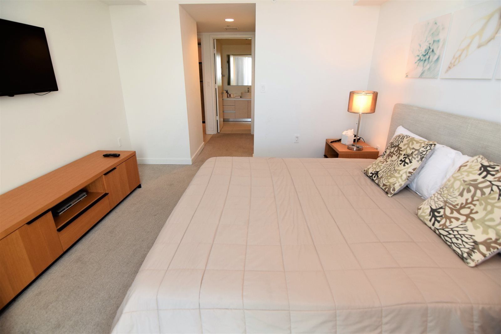 Een slaapkamer met een bed, een televisie, een nachtkastje met een lamp en een zichtbare badkamer door een geopende deur.