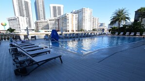 Un espace piscine aménagé sur le toit, avec des chaises longues et une vue sur les grands immeubles qui se dressent à l'arrière-plan.