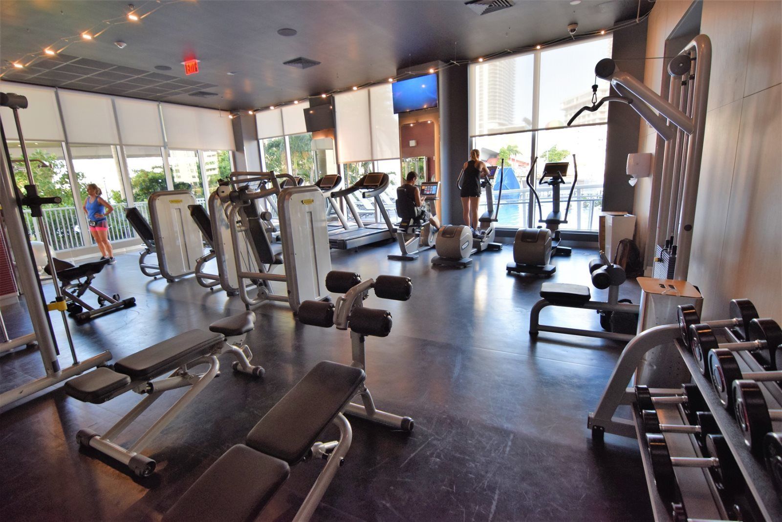 A gym with various exercise equipment, large windows, and a view of the outdoors.