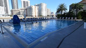 En swimmingpool med solstolar och en stadsbild i bakgrunden.