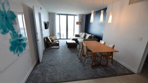 Ett modernt vardagsrum med en soffa, ett matbord med stolar, en tv som är monterad på väggen och ett stort fönster med gardiner.