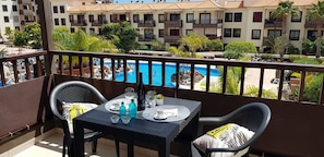 Ein Balkon mit einem Tisch für zwei Personen, Blick auf einen Pool und ein Gebäude mit Balkonen.