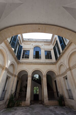 Un patio con un arco central, suelo de piedra y vistas a un edificio con múltiples ventanas y balcones.
