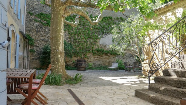 Un patio con una mesa y sillas de piedra, un árbol grande y una escalera.