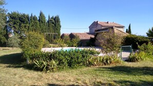 Una casa de piedra con techo de tejas, rodeada de césped y una piscina.