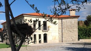 Um edifício de pedra com telhado de telhas vermelhas, varanda e pátio com brita.