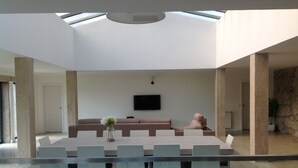Uma sala de estar espaçosa, com teto alto, mesa de vidro grande e um confortável conjunto de assentos.