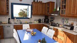 A kitchen with wooden cabinets, a blue table, and a view of the sea through a window. - Naxos is the Way Summer Dream 1 apartment (Kastraki)