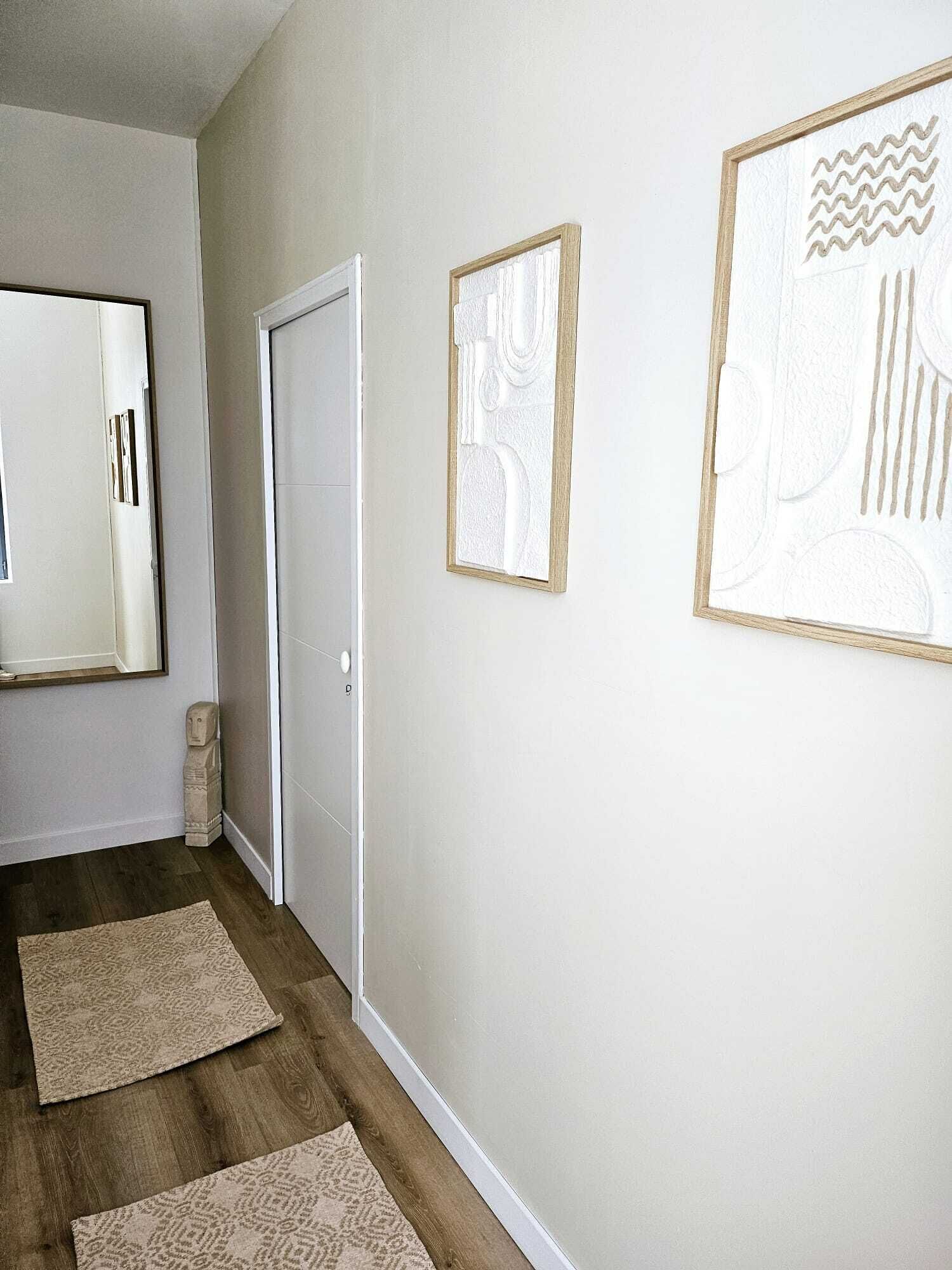 A hallway with a wooden floor, a white door, and two framed artworks on the wall.