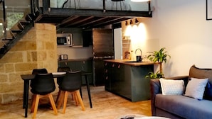 Et moderne opholdsrum med en trappe til et øvre plan, et spiseområde med sorte stole, en sofa med hynder og et sofabord.