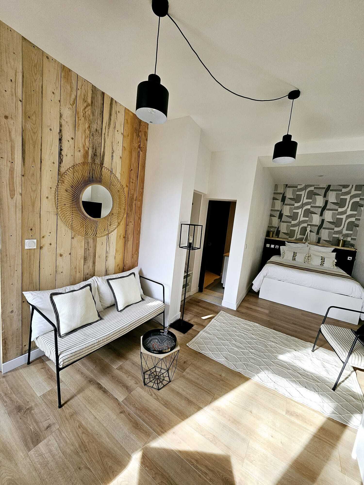 A modern living room with a wooden accent wall, a round mirror, a sofa, and a bed with patterned wallpaper.