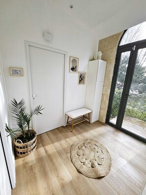 A room with a wooden floor, a white bench, a woven basket with a plant, and a round woven rug. - La Maison Grivolas (Avignon)