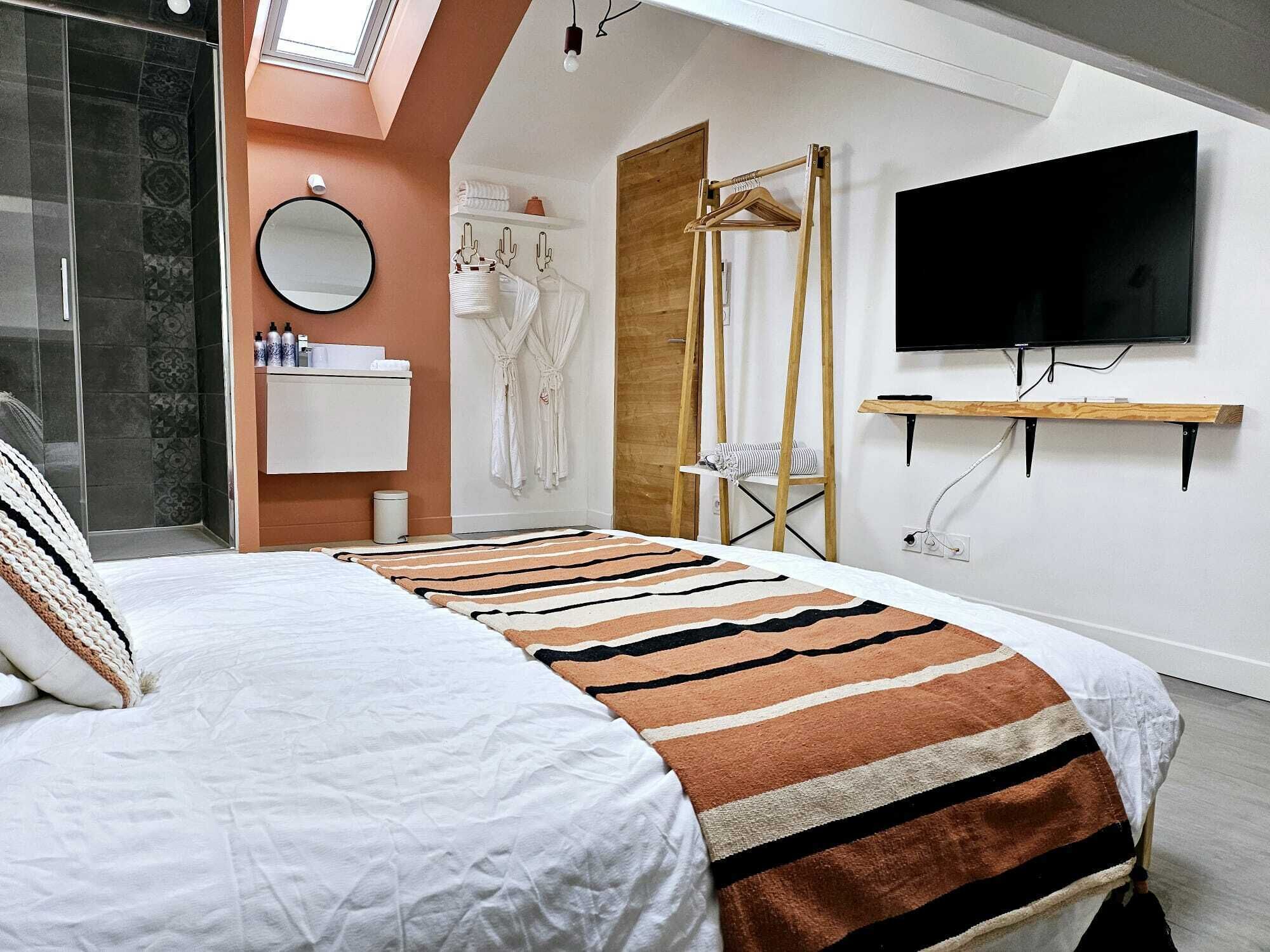 Ein modernes Schlafzimmer mit Bett, Fernseher, Spiegel, Schminktisch und Dusche.