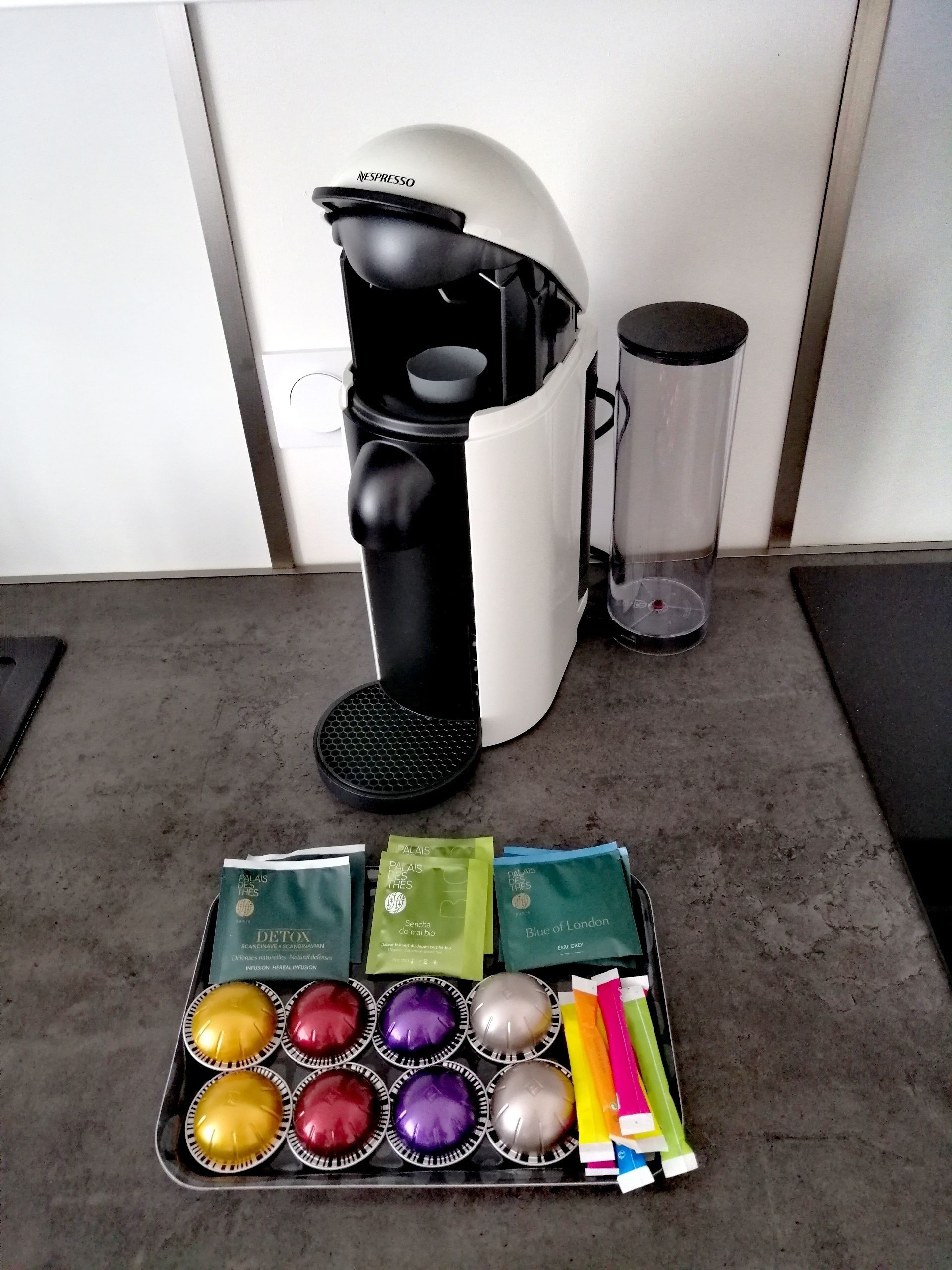 Eine Kaffeemaschine, ein Glasbehälter und eine Ablage mit verschiedenen farbigen Kapseln und Röhrchen.