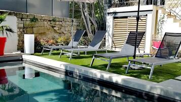 Una piscina con sillas de descanso y sombrillas, rodeada por un muro de piedra y vegetación.