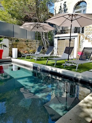 A swimming pool with lounge chairs and umbrellas, surrounded by a stone wall and greenery. - La Maison Grivolas (Avignon)