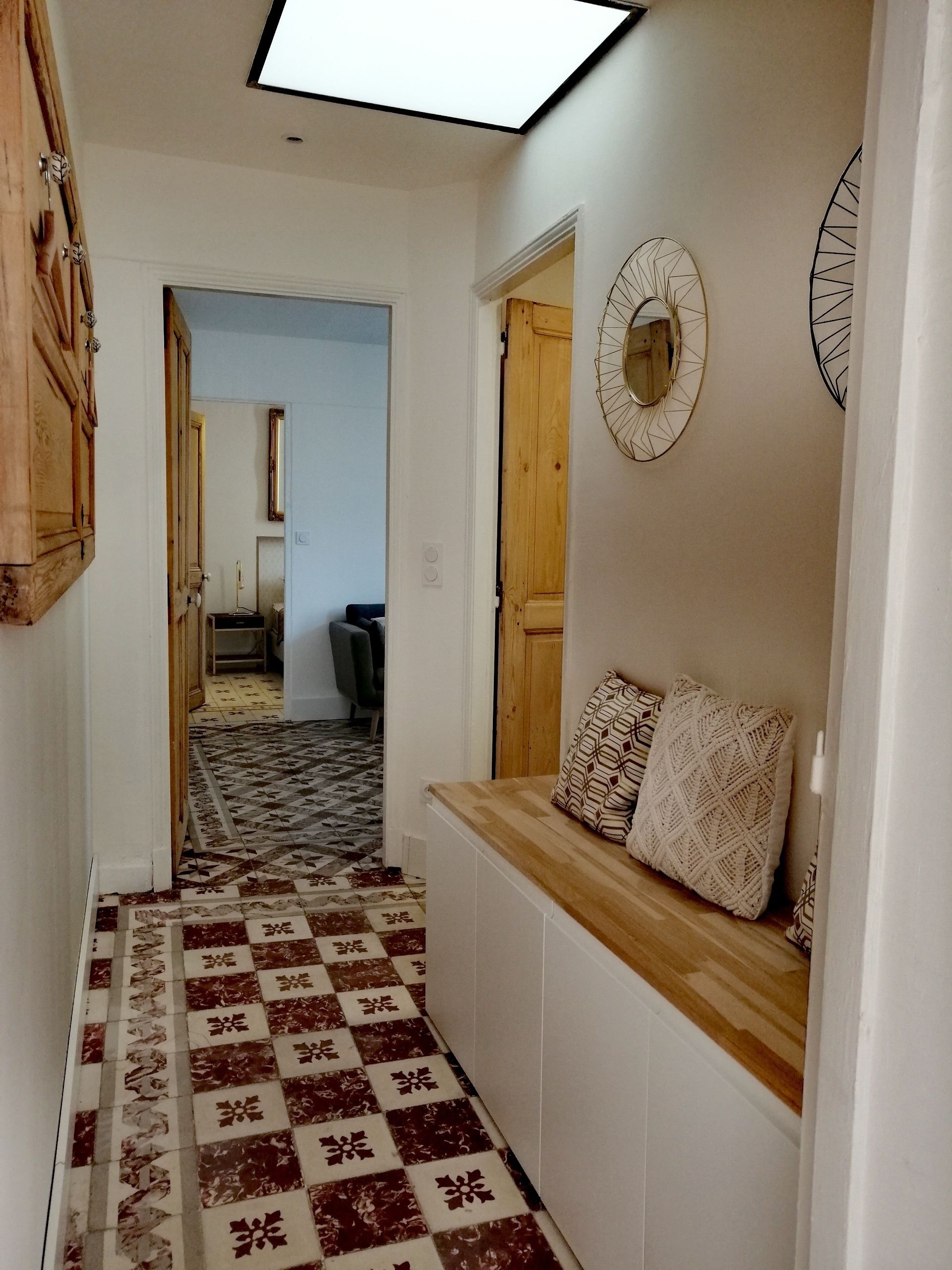 Un pasillo con suelo estampado, un banco de madera con cojines y un espejo decorativo en la pared.