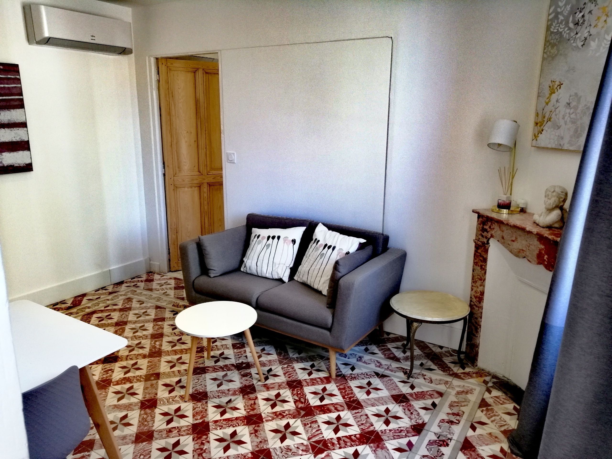 A small living area with a gray sofa, a round table, and a patterned floor.