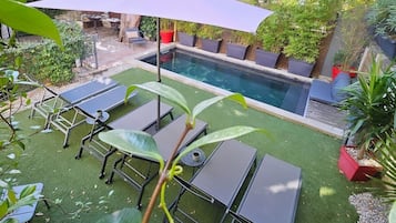 Relax by the serene pool surrounded by a lush garden with lounge chairs and a shaded seating area.