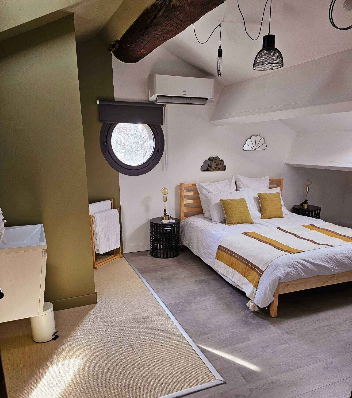 A bedroom with a large bed, a round window, a bedside table, and a nightstand.