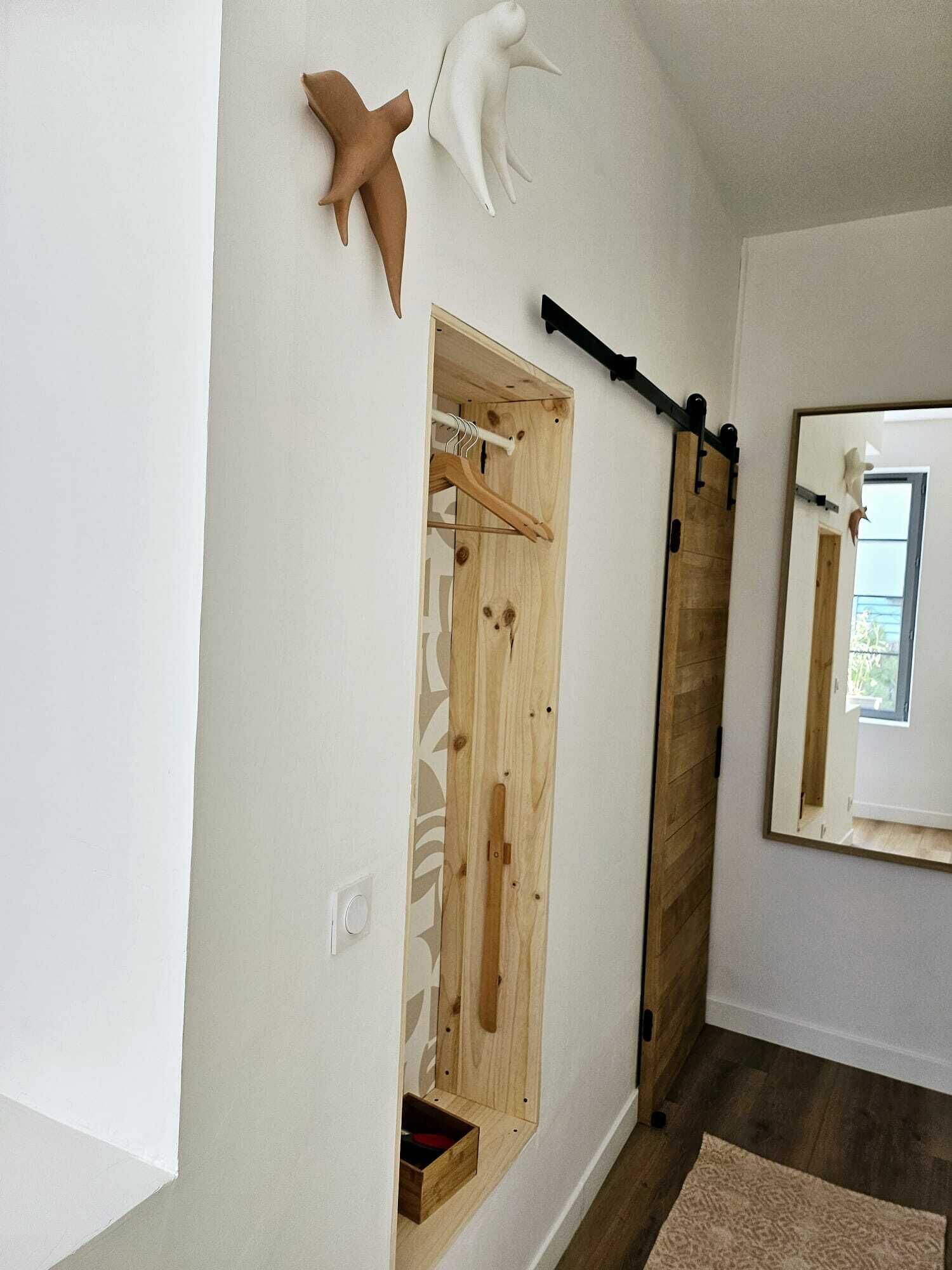 A room with a wooden wardrobe, a hanging rack, and a mirror.