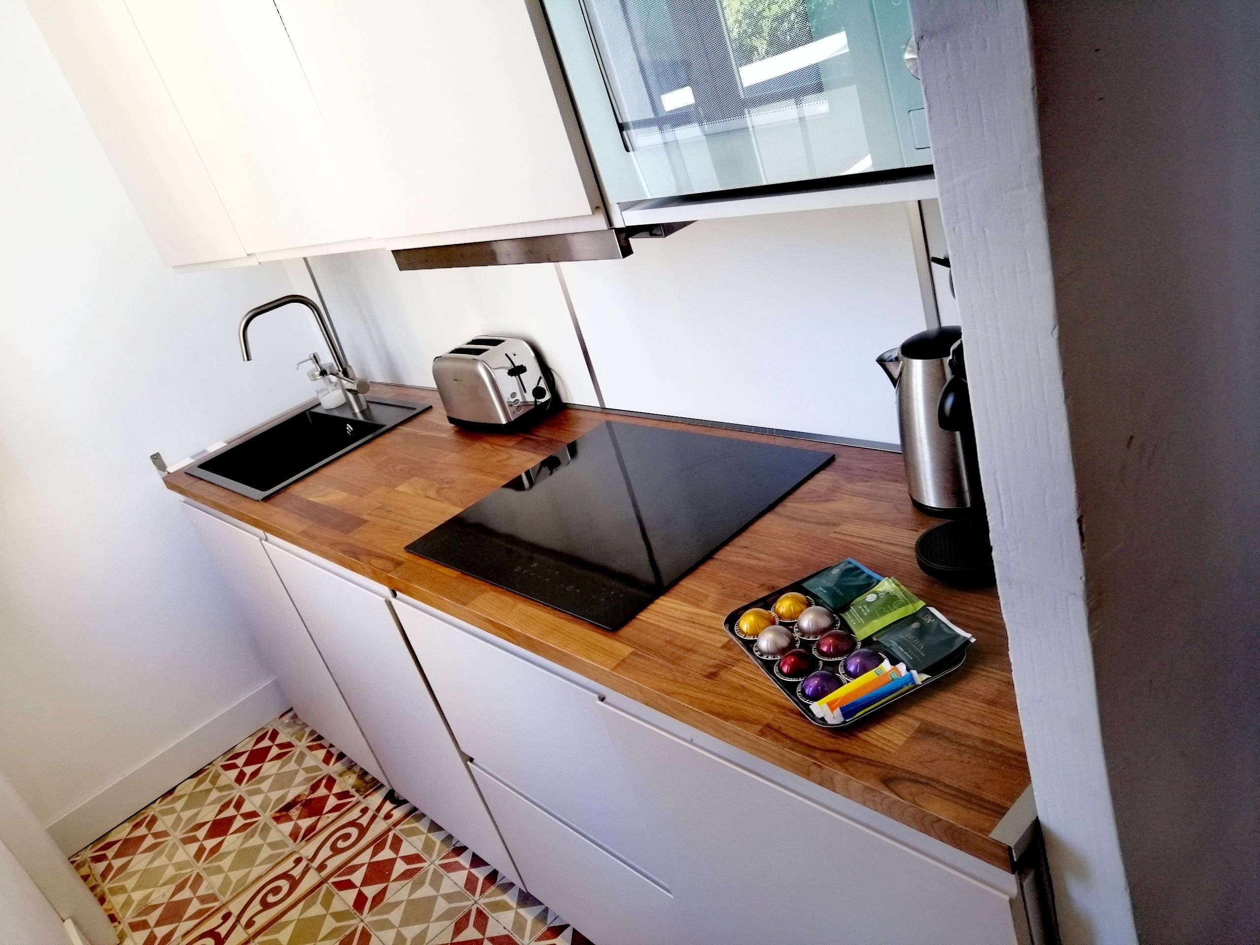 Une petite cuisine équipée d’un évier, d’un grille-pain, d’une bouilloire et d’un plateau rempli d’objets colorés.