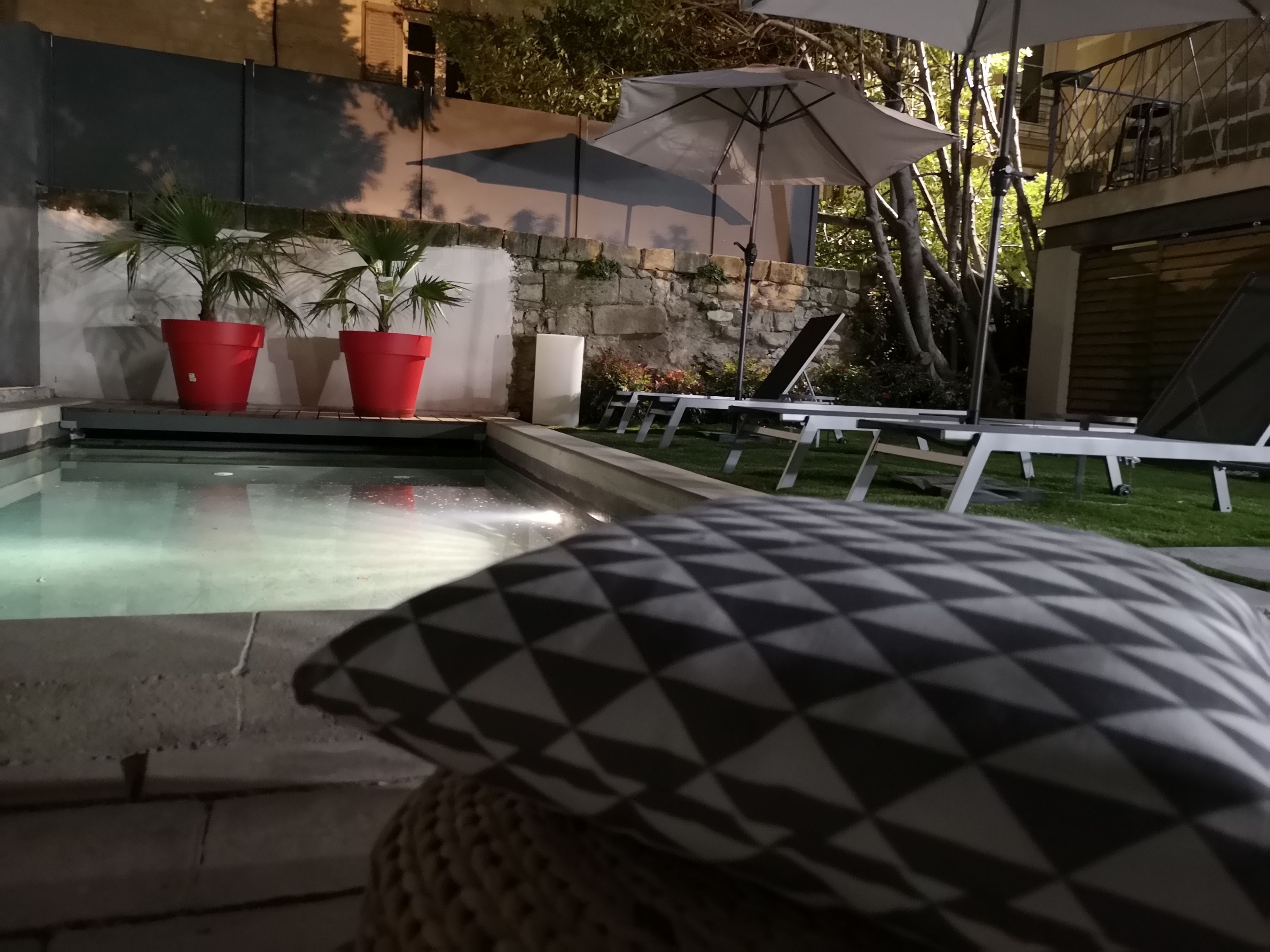 A pool area with lounge chairs and umbrellas, surrounded by stone walls and potted plants.
