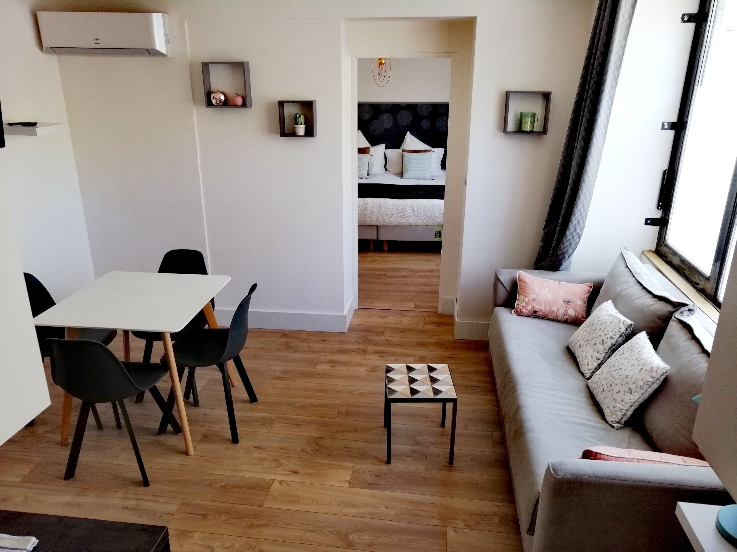 Un salon moderne avec un canapé, une table à manger et des chaises, une petite table d’appoint et un lit à l’arrière-plan.