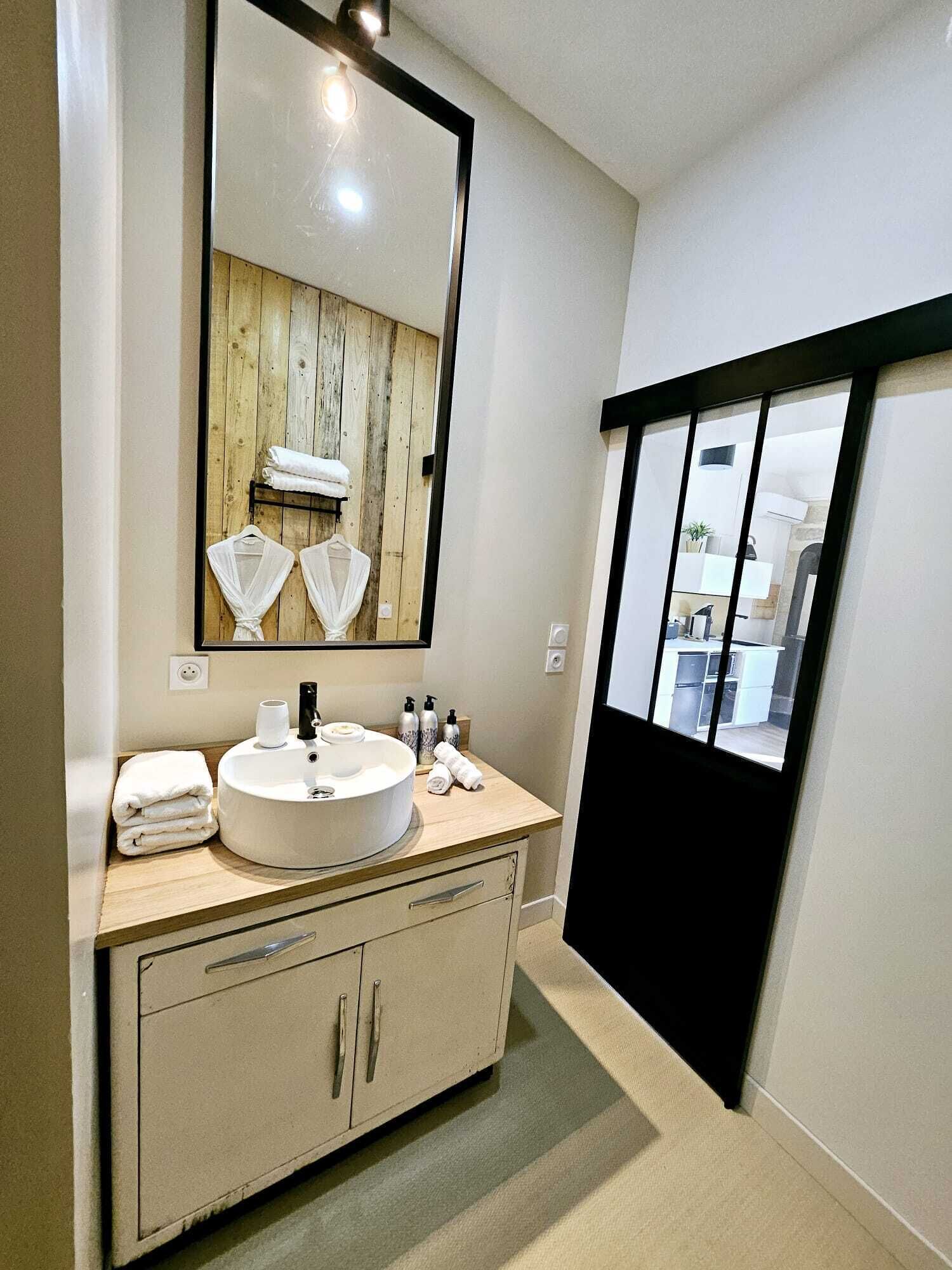 Une salle de bain moderne avec un grand miroir, un lavabo rond et un mur recouvert de panneaux en bois.