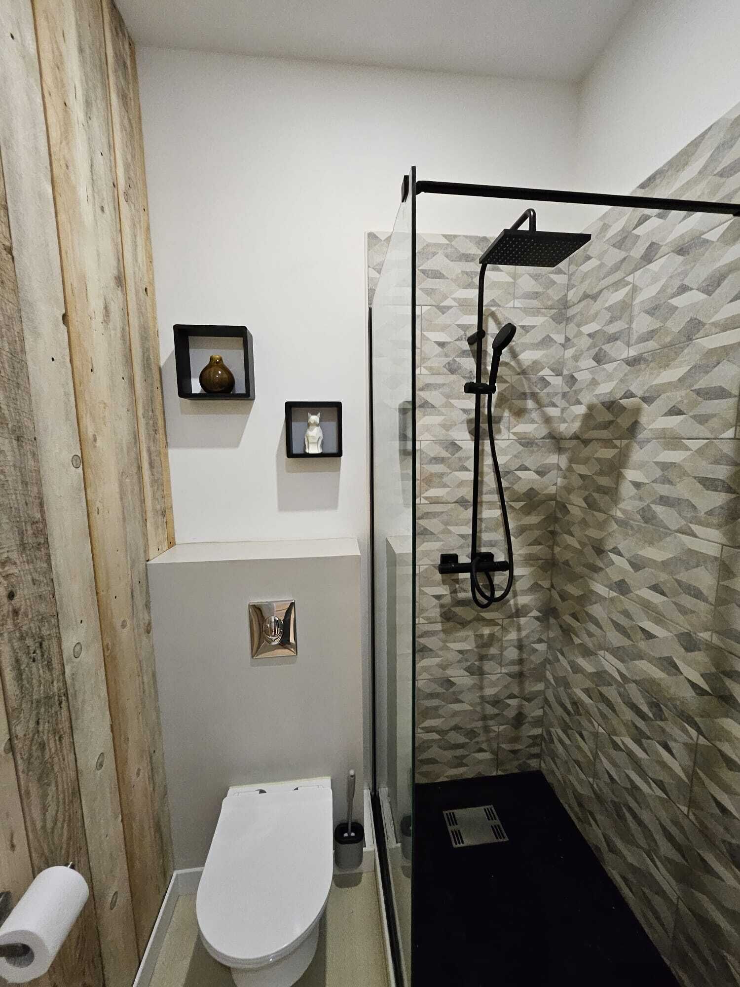A compact bathroom with a white toilet, a shower with a black hose, and a wooden wall.