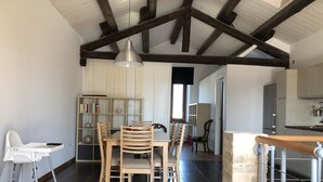 A spacious dining area with a high ceiling and exposed beams, a wooden dining table with chairs, a bookshelf, and a view into the kitchen area. - Linda apartment, 300 meters from the sea in a typical cottage perfect for families (Martinsicuro)