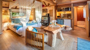 Un accogliente interno di una baita con un letto, un tavolo da pranzo in legno, angolo cottura e bagno.