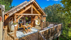 Una baita di legno con un patio, un'area pranzo con tavolo e sedie, e una sedia a dondolo.