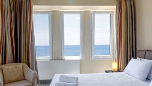 Et hotelværelse med seng, to vinduer med gardiner, en stol og et natbord med lampe.