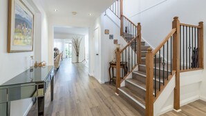 Ein geräumiger Flur mit einer Holztreppe, einem Glastischchen und gerahmten Kunstwerken an der Wand.