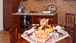 Eine Küche mit Holzschränken, einer Mikrowelle, einem Toaster und einem Spülbecken. Es gibt einen Tisch mit einem Korb voller Brot, Bananen und einem Teekessel.