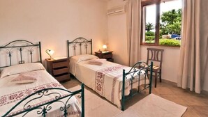 Ein Schlafzimmer mit zwei Einzelbetten, einem Nachttisch, einem Sessel und einem Fenster mit Vorhängen.