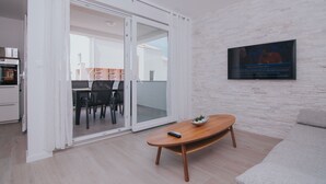 Una sala de estar moderna con un ventanal corredera que da a un balcón, una mesa de centro de madera y un televisor de pantalla plana montado en la pared.