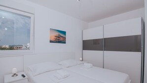 Una habitación de hotel moderna con una cama grande, una mesita de noche con una lámpara, un control remoto, toallas ordenadamente dobladas, un cuadro de una montaña y un armario.