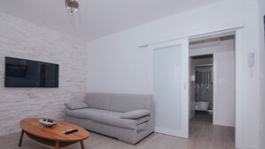 Una sala de estar moderna con un sofá gris, una mesa de centro de madera y un televisor de pantalla plana montado en una pared de ladrillo blanco.