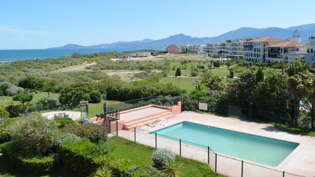 Area piscina con vista sul mare e sulle montagne, circondata dal verde e da un edificio con numerosi balconi.
